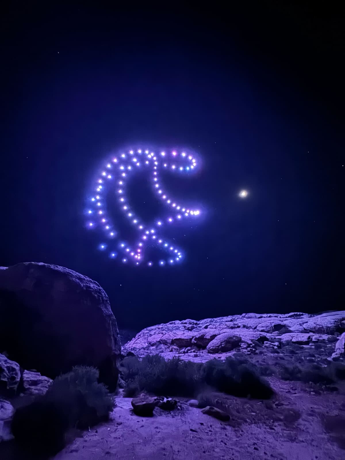 Crescent drone formation in purple light over Utah desert at night