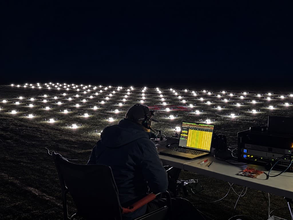 A crew member at the control station at night, the launch grid lit in rows on the field ahead