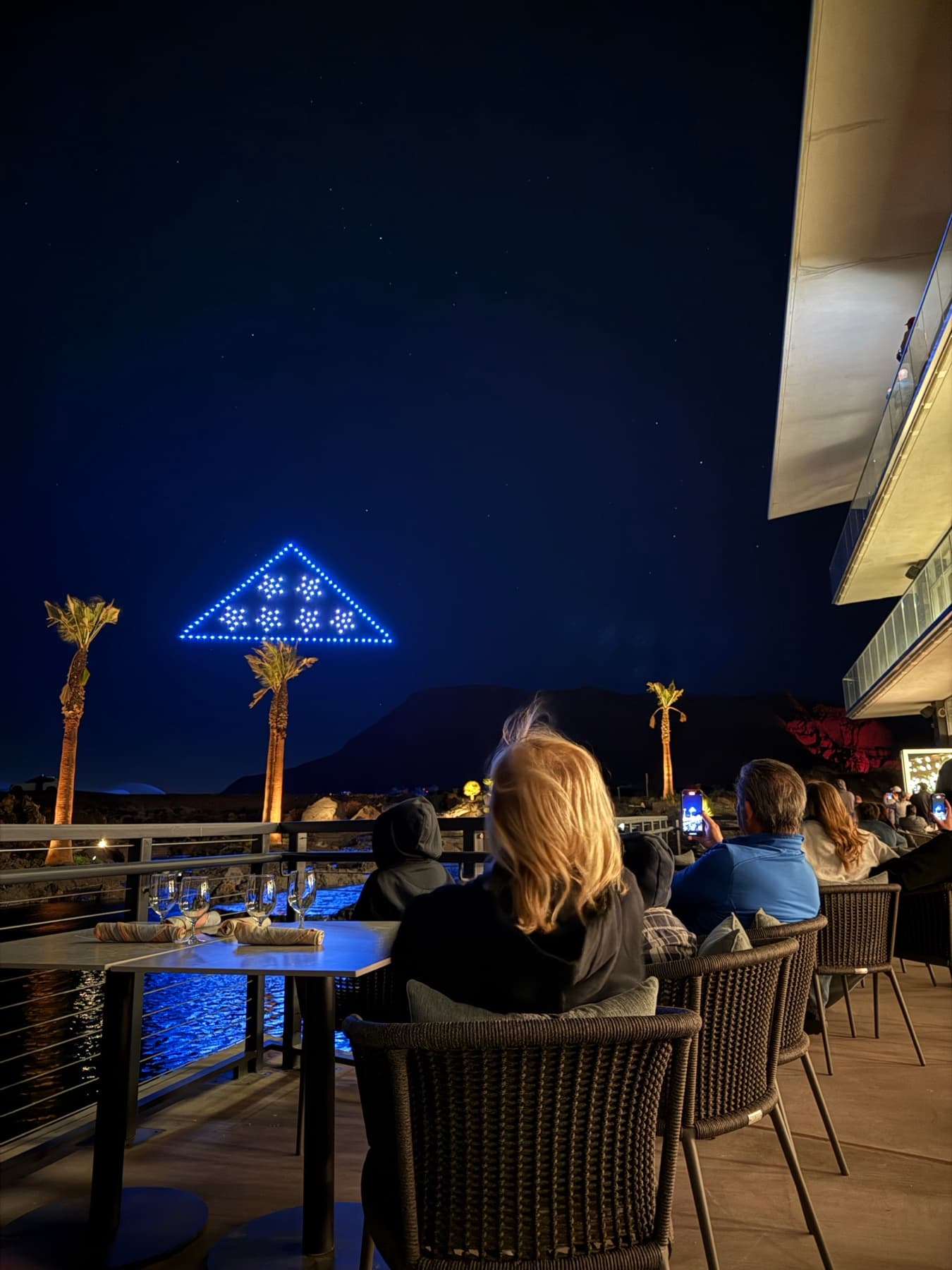 Guests watching a triangle drone formation from a dining terrace